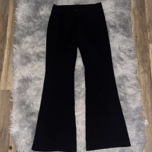 Svarta bootcut kostymbyxor RYVLS - Svarta kostymbyxor från RYVLS i bootcut-modell. Byxorna har hög midja, två bakfickor och stängs med dragkedja och knappar. Snygg passform och klassisk look, perfekta till en dressad outfit.