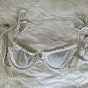 Vit bikiniöverdel med snörning, S - Vit bikiniöverdel med bygel och justerbara knytband vid axlarna. Stilren och enkel design utan mönster, tillverkad i stretchigt material med 80% nylon och 20% spandex. Perfekt för strand eller poolhäng i sommar. Storlek S!