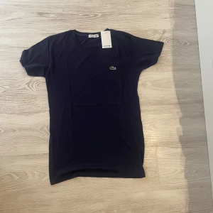 Mörkblå t-shirt från Lacoste - Snygg mörkblå t-shirt från Lacoste med klassisk krokodillogga broderad på bröstet. T-shirten har rund halsringning och korta ärmar. Tillverkad i mjuk bomull för en skön känsla och clean look.