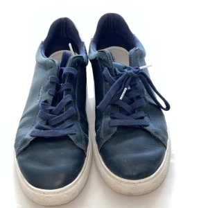 Marinblå sneakers från Gant - Snygga marinblå sneakers från Gant i skinn med vita sulor och blå snörning. Klassisk låg modell med rund tå och diskret Gant-logga på sidan. Yttersulan har coola detaljer i grönt och orange. Perfekta för en stilren och avslappnad look.