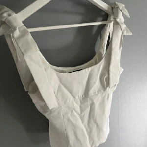 Vit korsettopp med knytband från Zara - Supersnygg vit korsettopp från Zara med breda axelband som knyts i rosetter. Toppen har en figurnära passform och fyrkantig ringning, perfekt att styla med jeans eller kjol. Aldrig använd!!💗