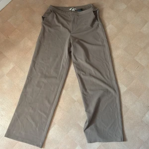 Beiga raka kostymbyxor från Zara - Snygga beiga byxor från Zara i rak modell. Byxorna har en enkel design med normal passform och är tillverkade i ett mjukt polyestertyg. Perfekta för en clean och stilren look.