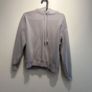 Grå hoodie från H&M med huva XS - En stilren grå hoodie från H&M i storlek XS. Tröjan har huva med snörning, ribbade muddar och en klassisk loose passform. Perfekt för chill dagar eller när du vill ha en enkel och snygg look.