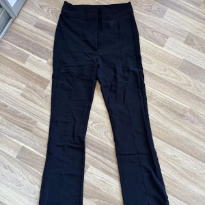 Svarta kostymbyxor från H&M Divided - Svarta kostymbyxor från H&M Divided i storlek 36. Byxorna har hög midja och lite bootcut ben med pressveck framtill. Materialet är mjukt och stretchigt för extra komfort.