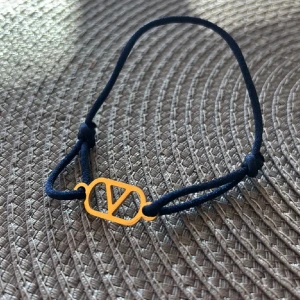 Valentino armband med blå snöre - Snyggt armband som liknar ett från Valentino med marinblått snöre och en guldfärgad metallbricka med det ikoniska V-logotypen. 