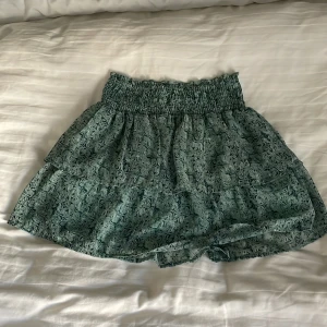 Grön blommig volangkjol med resår - Söt grönblå sommarkjol med ett fint mönster. Det är resårband i midjan vilket gör den stretchig. Köp gärna!