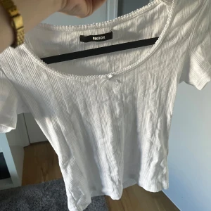 Jätte söt vit topp  - Supersöt vit ribbad topp från BikBok med kort ärm och liten rosett vid urringningen. Toppen har diskret hålmönster i ränder och en feminin, rundad halsringning. Perfekt att styla med jeans eller kjol för en fräsch look.