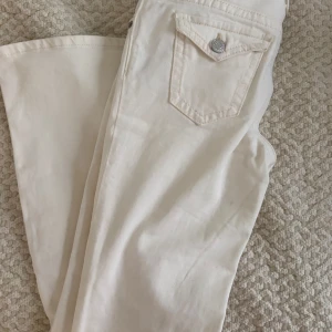 Vita bootcut jeans från H&M - Snygga vita jeans från H&M med bootcut-ben och låg midja. Byxorna har klassiska fickor med lock och silverfärgade knappar bak. Tillverkade i bomull för en skön känsla och stilren look. 146 storlek men kan passa som xxs