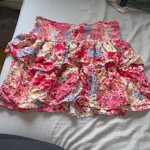 Blommig volangkjol 💐 - Supersöt kort volangkjol från Kappahl med blommigt mönster i rosa, rött, gult, lila och blått. Kjolen har smock i midjan och flera lager volanger som ger en flowy känsla. Perfekt för dig som vill sticka ut med färg och mönster i sommar.