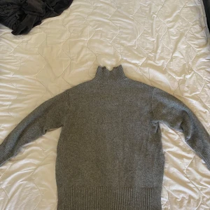 tjocktröja  - Mysig grå polotröja från H&M med hög krage och ribbade muddar. Tröjan är stickad och har en klassisk, enkel design som passar perfekt till lager-på-lager. Perfekt för kyliga dagar och enkel att matcha med jeans eller kjol.