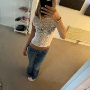 Vit spetsig croppad top med öppen rygg - Säljer en vit croppad blus i spets med fint mönster. Toppen är ärmlös och har en snygg öppen rygg som ger en extra touch. Perfekt att styla under en t-shirt, den svarta jag har på mig finns att köpa på min sida.