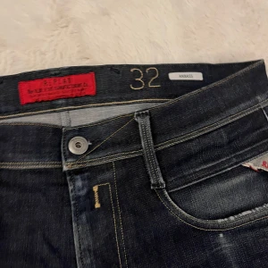 Replay Anbass jeans mörkblå, stl 32 - Snygga Replay Anbass jeans i mörkblå tvätt med klassiska kontrastsömmar och femficksdesign. Jeansen har en slim passform och raka ben, med läderpatch bak i midjan och diskreta slitningar för en cool look.