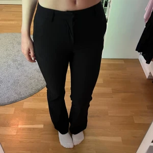 Svarta kostymbyxor med bootcut - Säljer ett par svarta kostymbyxor med bootcut-snitt och medelhög midja. Byxorna har hällor för bälte, fickor fram och är i ett mjukt, följsamt tyg som ger en snygg siluett. Perfekta för en clean och stilren look. Tyvärr för små på mig som ni kanske ser!