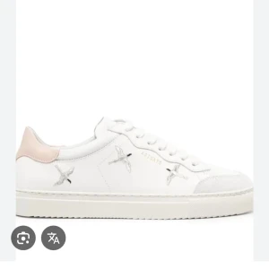 Vita sneakers från Axel Arigato - Stilrena vita sneakers i skinn från Axel Arigato med broderade fåglar på sidorna och en ljusrosa detalj vid hälen. Klassisk låg modell med snörning och platt sula. Perfekta för dig som gillar minimalistisk design med en twist. Storlek 38