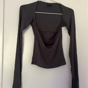 Grön långärmad topp Gina Tricot - Säljer en mörk grön (ljuset gör att den ser grå/svart ut) långärmad topp från Gina Tricot i storlek XS. Toppen har en snygg draperad urringning och är figurnära med stretchigt material. Perfekt att styla med jeans eller kjol för en trendig look.
