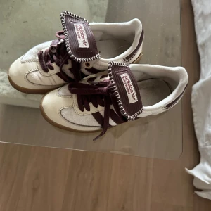Adidas Wales Bonner sneakers i vinrött och vitt - Adidas Wales bonner sneakers med vinröda detaljer och snörning. Ovandelen är i vitt med inslag av pälsliknande material och vinröda ränder samt häl. Klassisk gummisula och bred plös med Adidas-logga. Köpt vintage så har inte låda osv.