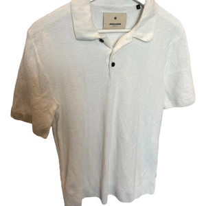 Vit piké från Jack & Jones Premium 10/10 skick - Snygg vit pikétröja från Jack & Jones Premium med klassisk krage och två svarta knappar. T-shirten har korta ärmar och är tillverkad i ett strukturerat bomullstyg som ger en schysst känsla. Perfekt för dig som gillar stilrena och enkla plagg.😁 Aldrig använd bara testad😁skick 10/10👍