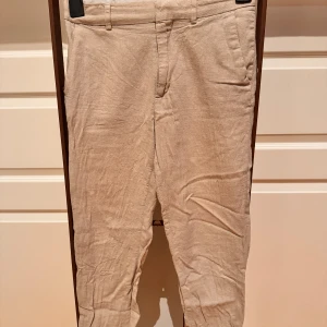 Beiga linnebyxor med normal passform - Snygga beiga linnebyxor med klassisk design och normal passform. Byxorna har fickor i sidorna, bälteshällor och stängs med dragkedja och knapp. Perfekta för en avslappnad och stilren look under varmare dagar.