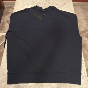 Mörkblå tröja från J.Lindeberg - Snygg mörkblå crewneck från J.Lindeberg med diskret logga på bröstet. Tröjan har rund halsringning och är tillverkad i mjuk bomull. Perfekt för dig som gillar stilrena och klassiska plagg med en modern touch. Plagget är aldrig använt och är köpt på Nk. Den passar Både Large och Medium i mitt tycke. Den är köpt för 1800 och jag säljer den för 649 vilket är ett väldigt bra pris! Priset är diskuterbart vid snabb affär! Skriv vid vilken fråga som helst!