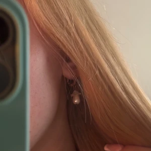 Guldiga örhängen med pärldroppar - Superfina örhängen med guldfärgade ringar och hängande vita pärldroppar formade som små blommor. Perfekt för dig som gillar unika detaljer och vill ha något som sticker ut. Ger en söt och elegant känsla!