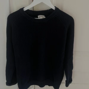 Mörkblå stickad tröja från East West - En enkel och stilren mörkblå stickad tröja från East West. Tröjan har rund halsringning och långa ärmar, perfekt för kyliga dagar. Den grova stickningen ger en mysig känsla och passar bra till jeans eller kjol.