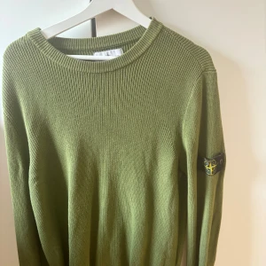 Olivgrön Stone Island tröja stickad - Säljer en olivgrön stickad tröja från Stone Island med klassisk patch på ärmen. Tröjan har rund halsringning och är ribbstickad i hela plagget. 