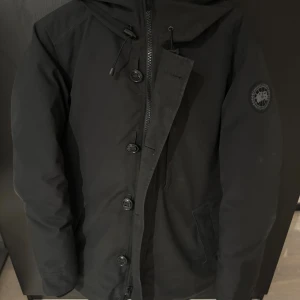 Canada goose black label - Säljer en unik vinterjacka från Canada Goose med huva och klassisk logga på ärmen. Jackan säljs inte längre och nypris på den ligger runt 17k. Jackan har både dragkedja och knappar framtill, samt två fickor på sidorna. Perfekt för kalla dagar och riktigt snygg streetstil. Den är väldigt fräsch och passar till M och L 