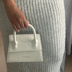Vit handväska från Fashion & YM - Säljer en stilren vit handväska från Fashion & YM med struktur i syntetmaterial. Väskan har två handtag, guldiga metalldetaljer och ett huvudfack med dragkedja inuti. Perfekt storlek för det viktigaste och ger en clean look till din outfit. Dessvärre har väskan band ett fläck på innersidan, inget som syns men kan vara bra att känna til! :)