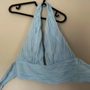 Ljusblå halterneck topp - Supersnygg ljusblå halterneck topp med långa knytband. Toppen har en rynkad struktur och är ärmlös, perfekt för varma dagar. Passar även L/XL då man själv kan justera i ryggen