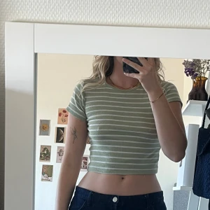 Grön och vit randig croppad topp - Superfin croppad topp i ljusgrönt och vitt med horisontella ränder. T-shirten har korta ärmar, rund halsringning. Nopprig över hela men inget man direkt tänker på, då det är ungefär samma över hela 