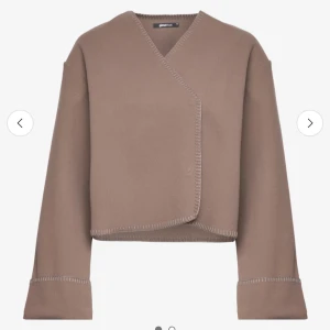 Beige omlottkofta från Gina Tricot - Säljer en beige omlottkofta från Gina Tricot med markerade sömmar och v-ringad hals. Koftan har lång ärm och en croppad passform som ger en modern look. Perfekt att styla med höga jeans eller kjol.