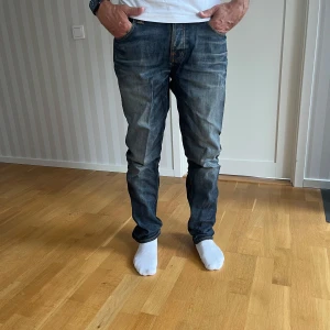 Nudie jeans: GRIM TIM - Säljer ett par nudie jeans grim Tim jeans, i wornin pepper tvätt och klassiska kontrastsömmar. Modellen har raka ben och normal passform, med 5 fickor och logga på bakfickan. Stretchigt jeanstyg för extra komfort.    I strl W33 L34