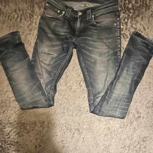 Nudie Jeans blå W24 L30 - Snygga jeans från Nudie Jeans i tvättad blå färg med slitningar och klassiska bakfickor med vågig söm. Perfekta till sneakers eller boots. Materialet är mjukt och stretchigt jeans.
