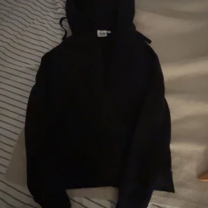 Svart hoodie från Frank Dandy - Svart hoodie från Frank Dandy med klassisk huva och dragsko. Tröjan har lång ärm och en enkel, stilren design utan tryck. Perfekt för dig som gillar en clean och avslappnad look.