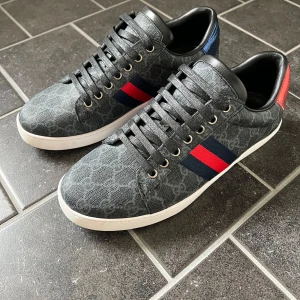 Gucci ace - Snygga Gucci ace i svart med klassiskt GG-mönster, blå och röda ränder på sidorna samt röd och blå häl i ormskinnslook. De är i otroligt bra skick 9,5/10 då jag använt dom 2-3 gånger. Dom är för små för mig därför jag säljer dom. Säljer för 3 499kr men vid snabb affär sänks de mer då jag bara vill bli av med dom. Box, kvitto osv ingår.