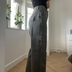 Khaki cargopants från A-DSGN - Snygga gröna cargopants från A-DSGN med raka ben och flera snygga fickor på sidorna och bak. Byxorna är använda 5 gånger, men fint skick
