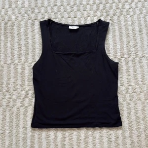 Svart linne med breda axelband från Gina Tricot - En svart, enkel och stilren linnetopp från Gina Tricot, basically basics-kollektionen. Toppen har en rak, något tight passform och ärmlös design med fyrkantig ringning. På nedredelen av baksidan är det två små hål (se sista bilder)