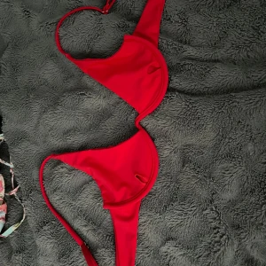 Röd bikini med metallspänne - Snygg röd bikini med trekantsformad överdel och matchande underdel. Båda delarna har coola metallspännen och smala band. Perfekt för stranden eller poolen. Materialet känns mjukt och stretchigt, troligtvis syntet. Enkel och stilren design utan mönster. Vid frågor hör av dig!