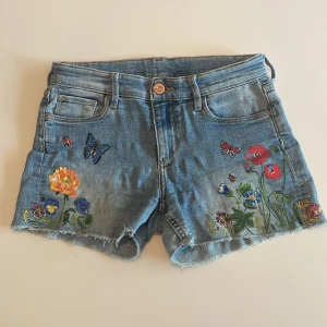Blommiga jeansshorts H&M 🌷🌿💕 - Snygga ljusblå jeansshorts med rå kant från H&M x Nathalie Lété. Framsidan har färgglada blommor, fjärilar och nyckelpigor tryckta på tyget. Klassisk femficksmodell och knappstängning. Perfekta för dig som gillar unika detaljer och somrig vibe. Jeansen är i strl 140, men skulle säga att de är större och passar åtminstone 150💋De är mid/low waist, och suuuper fina💕🪽🤩
