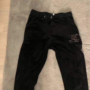 Svarta mjukisbyxor Juicy Couture - Svarta mjukisbyxor från Juicy Couture med klassisk logga på höften. Byxorna har snörning i midjan och två bakfickor. 