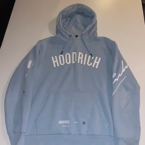 Ljusblå hoodie från Hoodrich - Säljer en ljusblå hoodie från Hoodrich med vit logga framtill och tryck på ärm och rygg. Tröjan har huva med snörning och en stor magficka. Perfekt för dig som gillar streetwear och vill sticka ut med snygga detaljer. Den är också i bra skick ej andvänd så många gånger.(Limeted edition)