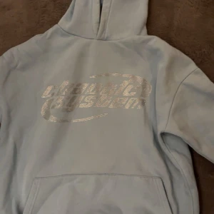 Ljusblå hoodie från FSBN med tryck - Säljer en ljusblå hoodie från FSBN i relaxed fit med silvrigt tryck på bröstet där det står 'chaotic system'. Tröjan har huva, magficka och är fodrad med mjukt material på insidan. Perfekt för dig som gillar streetwear vibes. ✨