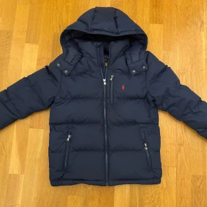 Mörkblå dunjacka Polo Ralph Lauren - Snygg mörkblå dunjacka från Polo Ralph Lauren med huva. Köpt på kids Brand store och har haft den en vinter säsong vilket resulterar att det är mycket bra skick🤩 storlek 14/16 år