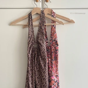 Mönstrad halterneckklännig från urban outfitters - Säljer två snygga halterneckklänningar i mjukt, glansigt material. Ena klänningen är brun med beige abstrakt mönster, den andra har ett rosa, svart och beige mönster med splash-effekt. Båda har ringdetalj framtill och djup rygg. Perfekt för dig som vill sticka ut! Säljer 2 för 300kr eller 1 för 200kr.