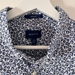 Blommig skjorta från Gant XL - Snygg skjorta från Gant i storlek XL med blommigt mönster i blått och vitt. Skjortan har klassisk krage, knäppning framtill och långa ärmar. Perfekt för dig som vill sticka ut med en fräsch och modern look.