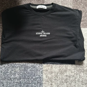 Svart Stone Island Archivio t-shirt - Svart t-shirt från Stone Island med ARCHIVIO-tryck på bröstet och unik print på ryggen. Klassisk rund hals och korta ärmar. Materialet är mjukt och skönt, perfekt för dig som gillar streetwear med exklusiv känsla. Priset går att diskuteras såklart. ÄKTA BTW!!!!