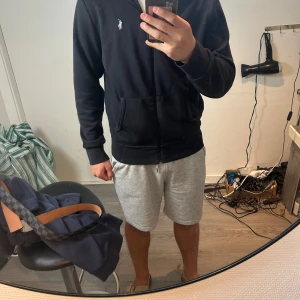 Svart hoodie från Polo Ralph Lauren - Svart hoodie från Polo Ralph Lauren med dragkedja framtill och klassisk broderad logga på bröstet. Tröjan har huva, känguruficka och är tillverkad i mjuk bomull. Perfekt för chill dagar eller när du vill ha en clean och stilren look.