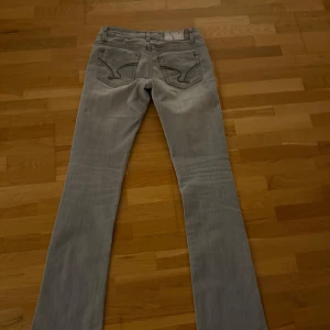 Grå jeans från Big iteno - Snygga ljusgrå jeans från Big iteno med botcut  ben och coola broderade detaljer på fickorna. Jeansen har klassisk femficksdesign, silverfärgade nitar och subtila slitningar framtill. Perfekta för dig som gillar en stilren men ändå unik look. Super fina  skriv vid minsta lilla funderingar 😜34 cm i midjemått rakt över  81-82 cm i innerbenet 