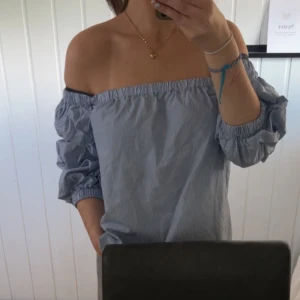 Blåvit offshoulder topp från H&M - Säljer en blåvit randig offshoulder topp från H&M i storlek 38. Toppen har puffiga trekvartsärmar med resår och är tillverkad i mjuk bomull. Perfekt för dig som gillar en chill och trendig look med baraxlat och relaxed fit.