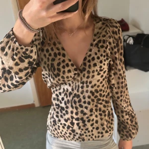 Leopardmönstrad omlottblus från H&M - Säljer en  leopardmönstrad omlottblus från H&M i storlek XS. Blusen har v-ringning, långa småpuffiga ärmar och knyt i midjan för en valfri passform.